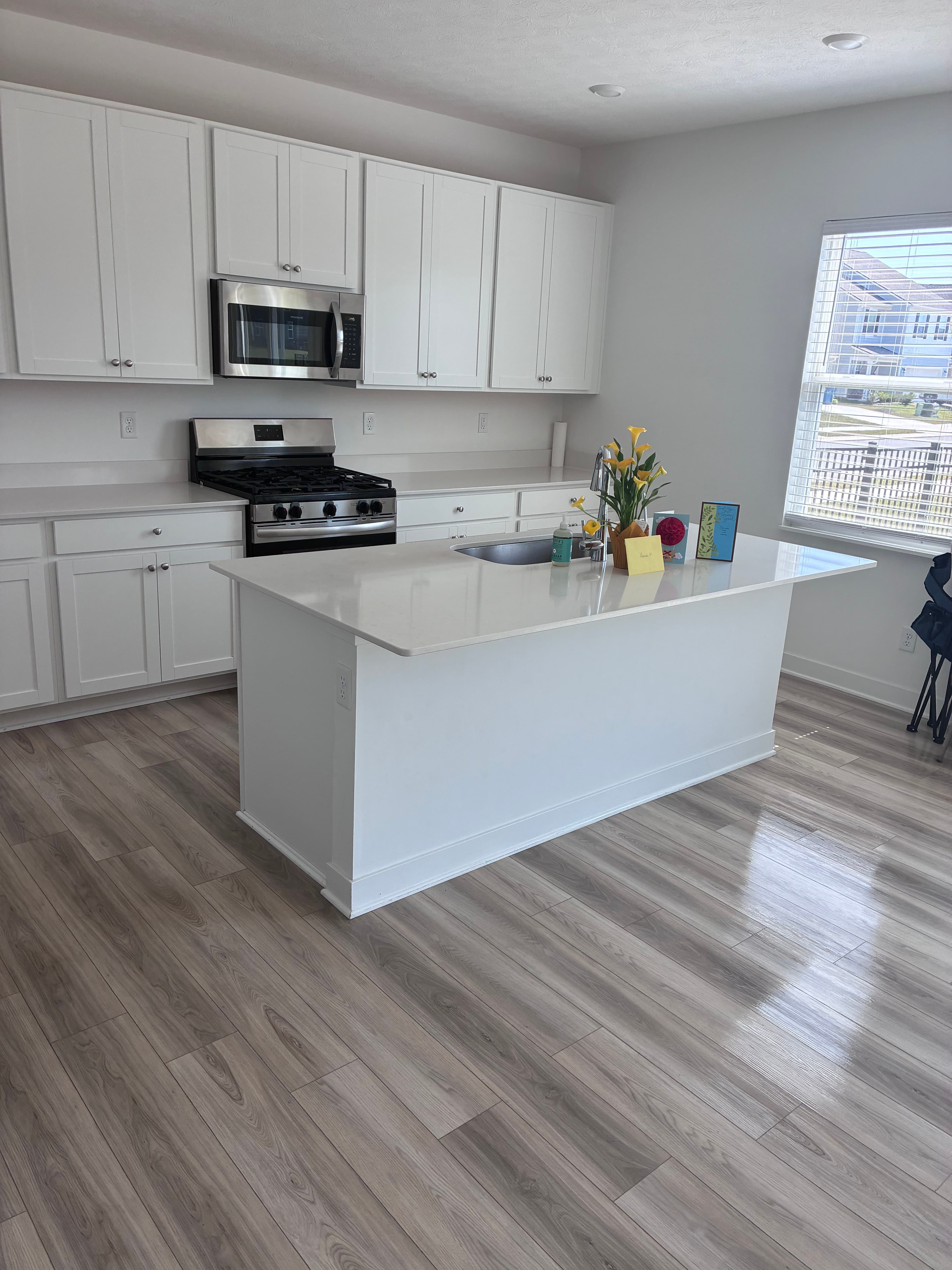 Modern white kitchen featuring stainless steel appliances, a large island, and light wood-look flooring.
